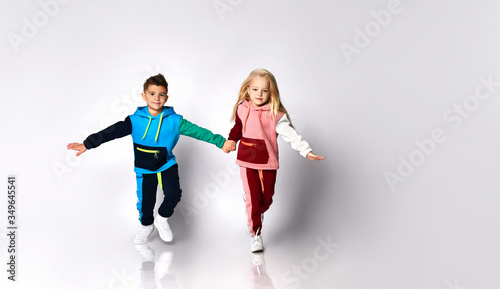 Children, boy and girl, in colorful sport suits and sneakers. They are holding hands, running, isolated on white studio background