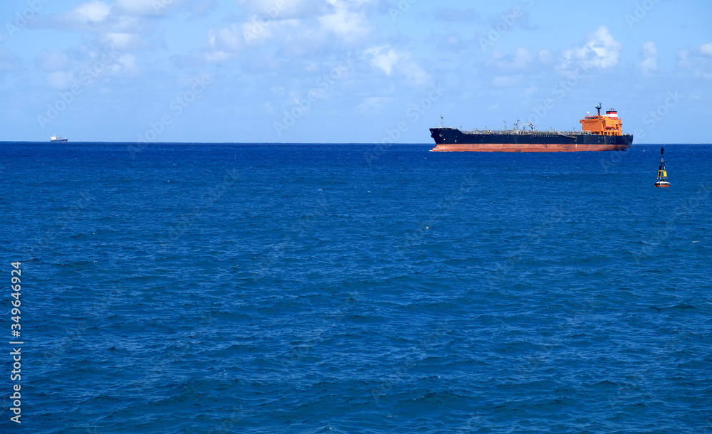 A tanker cargo ship on the sea, passing by a cardinal navigation buoy.
