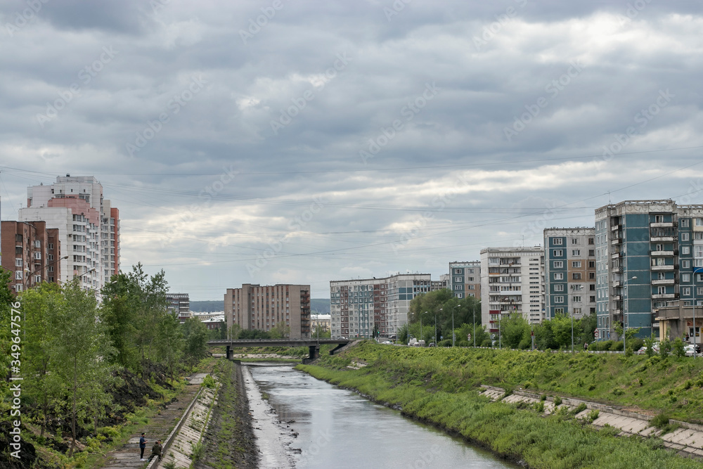 A small river in the city and a bridge over the river. Cityscape with old houses and cloudy skies.