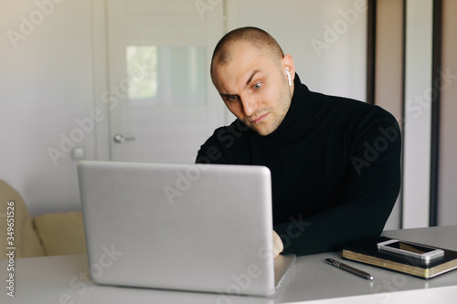 Surprised short haired man sitting at tablework at laptop thinking of problem solution, thoughtful male employee pondering considering idea looking at computer screen making decision