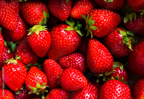 Red biological strawberry background. Many bright fresh berries with green leaves. Horizontal harvesting composition. Seasonal fruits wallpaper. Raw food pattern. Vitamins and healthy eating products.