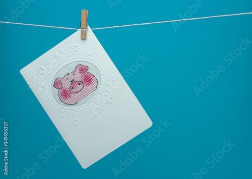Handmade cross-stitch postcard hanging on a rope with clothespin. Muzzle piggy.