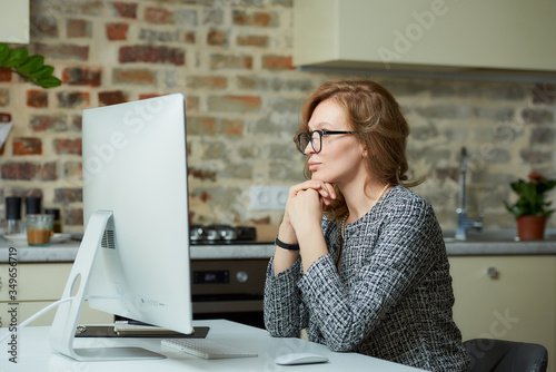 A pretty woman in glasses works remotely on a desktop computer in her studio. A female boss sits arms crossed at a video conference at home. A female student listening to an online lecture..