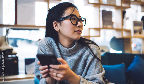 Fotografie Beautiful asian hipster girl in casual wear and spectacles resting on break usin