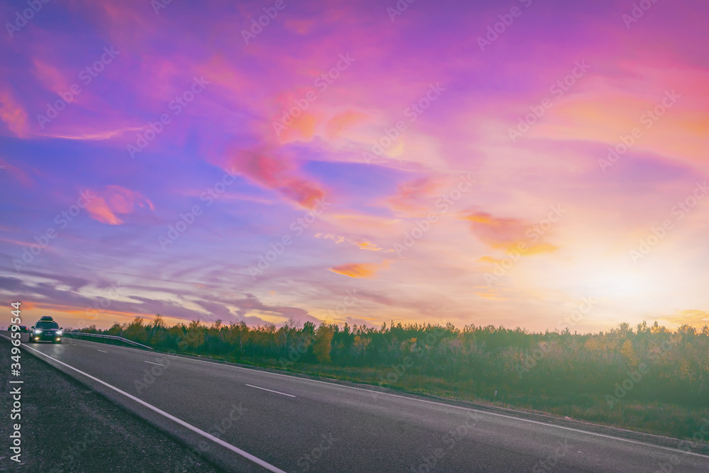 car in motion on the highway on the background of a beautiful colorful sky at sunset