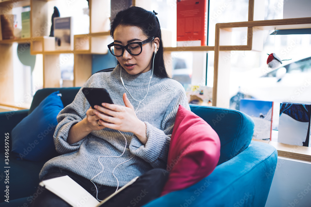 Obraz premium Focused Asian woman sitting on sofa with mobile phone