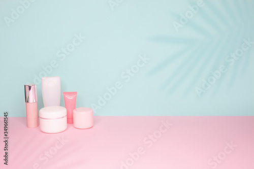 Side view on a still life. Different cosmetic bottles on a bright pink and mint background with palm leaves shadows . 