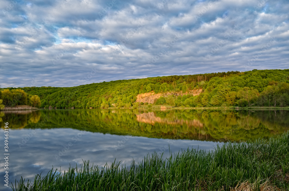 Landscape of a forest lake on a background of cloudy sky.