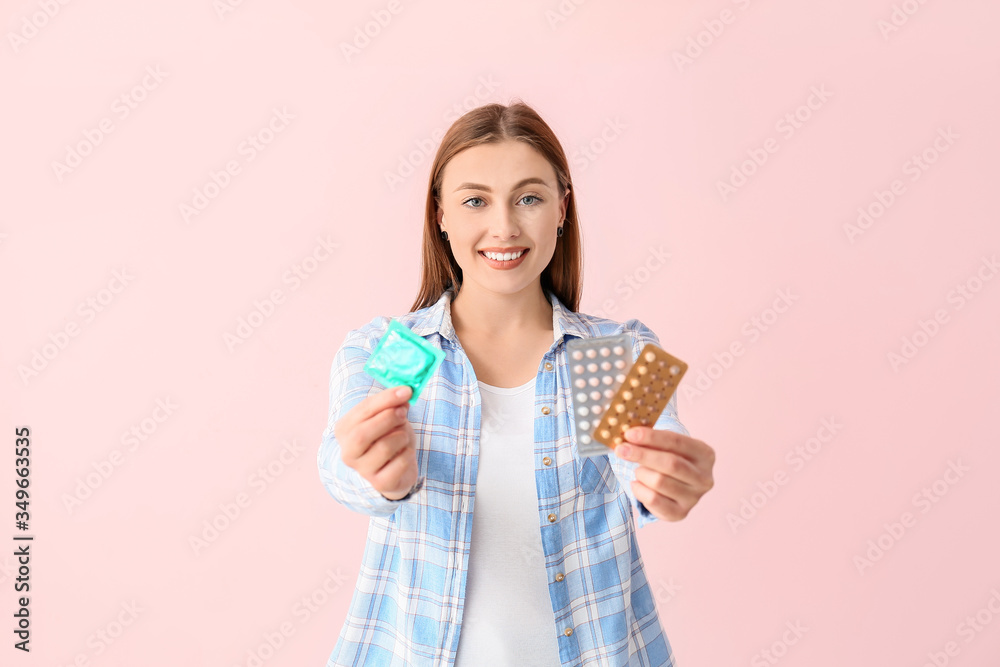 Young woman with condom and birth control pills on color background Young woman with condom and birth control pills on color background