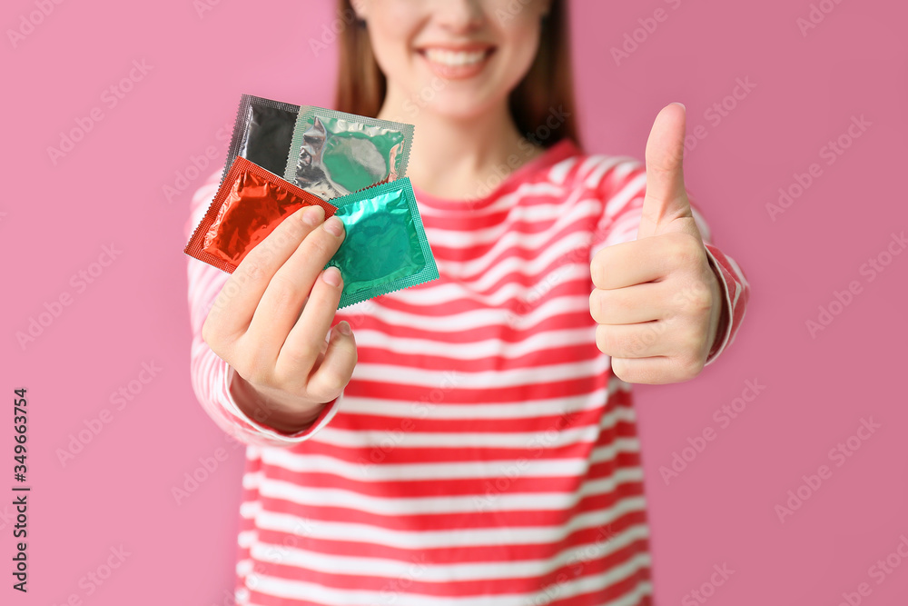 Young woman with condoms showing thumb-up on color background Young woman with condoms showing thumb-up on color background