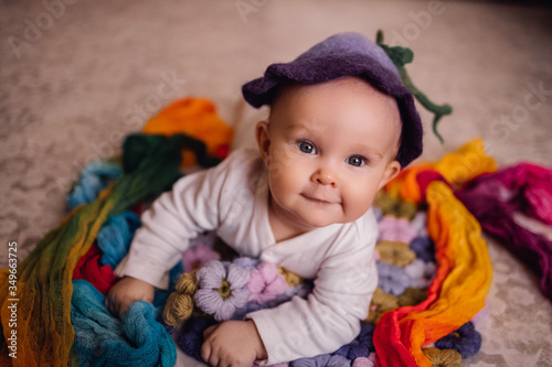Cute baby looking at camera. Child newborn smiles with open eyes with bell flower hat on head