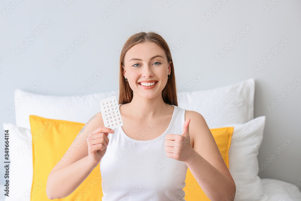 Young woman with birth control pills showing thumb-up at home Young woman with birth control pills showing thumb-up at home