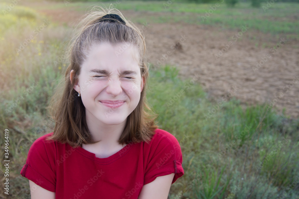 Young beautiful teenager girl squinting fun in a field outdoors. Copyspace.