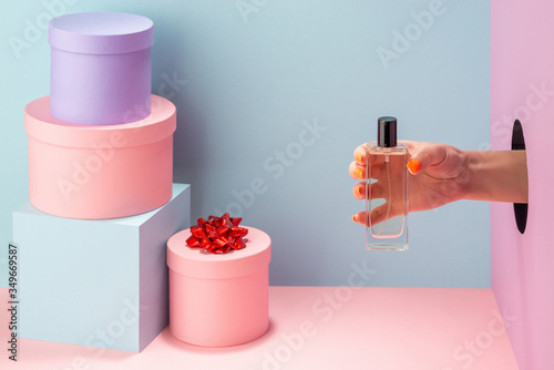 Woman's hand holding a bottle of perfume on blue and pink background