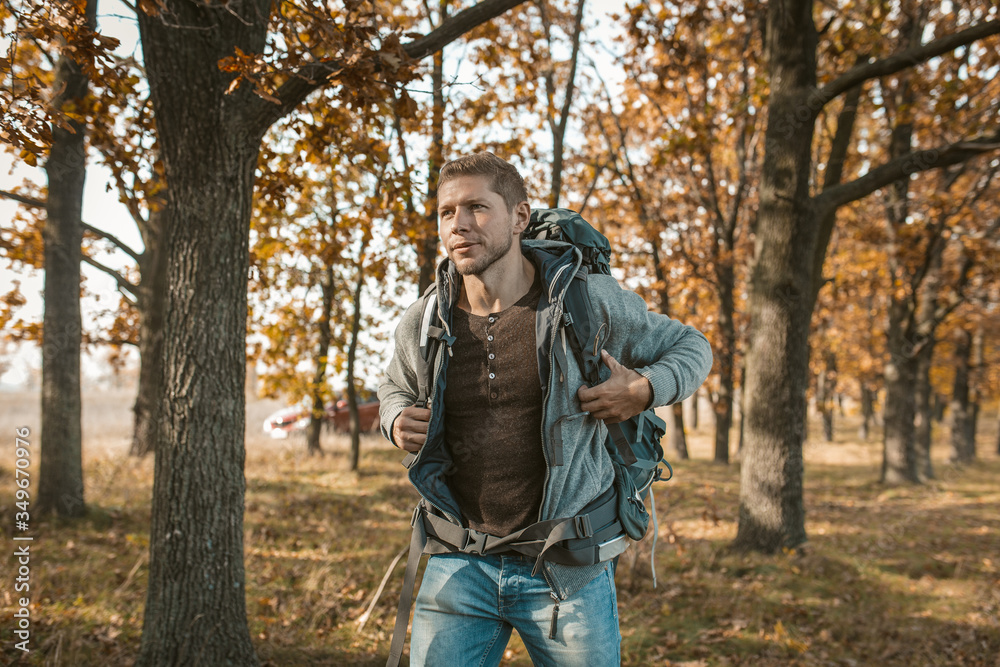 Tourist at the beginning of the journey. An inspired guy with a big backpack got out of a red car and begins his journey through the autumn forest. Hiking concept Tourist at the beginning of the journey. An inspired guy with a big backpack got out of a red car and begins his journey through the autumn forest. Hiking concept
