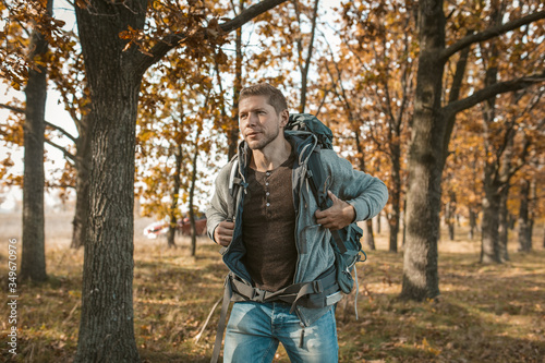 Tourist at the beginning of the journey. An inspired guy with a big backpack got out of a red car and begins his journey through the autumn forest. Hiking concept