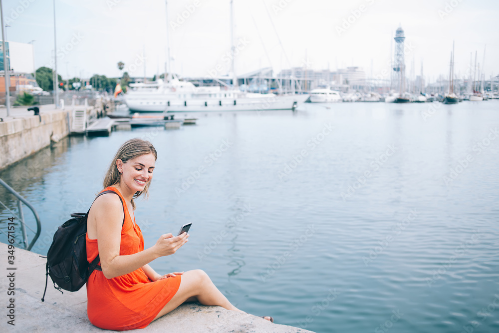 Joyful female traveler surfing Internet on smartphone in harbor