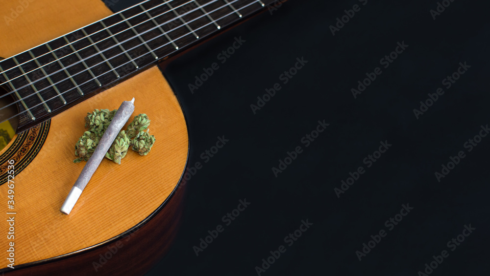 Fototapeta premium Big marijuana joint and cannabis buds on classic guitar isolated on black background. Copy space right. Concept of music and weed, inspiration, creativity...