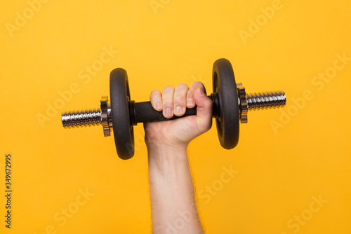 Working out concept. Cropped photo of a strong man holding dumbbell in hand isolated on yellow background