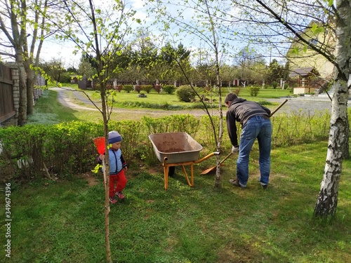 Father and little son work together in a garden with a rakes and a wheelbarrow. family teamwork