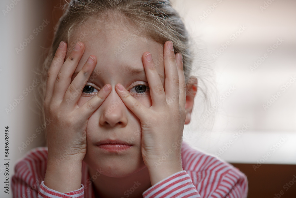 Fototapeta premium Close up of cute blond hair school girl boring and tired, holding her hand over the face, sad mood, cheerless unhappy kid, closed at home during quarantine 2020 