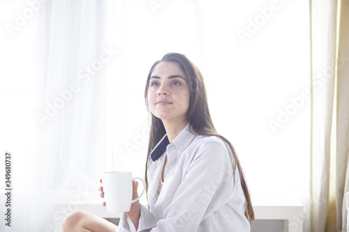 Young beautiful happy brunette woman in black silk dressing gown lying in bed, drinking morning coffee, white cup. Womens day holiday