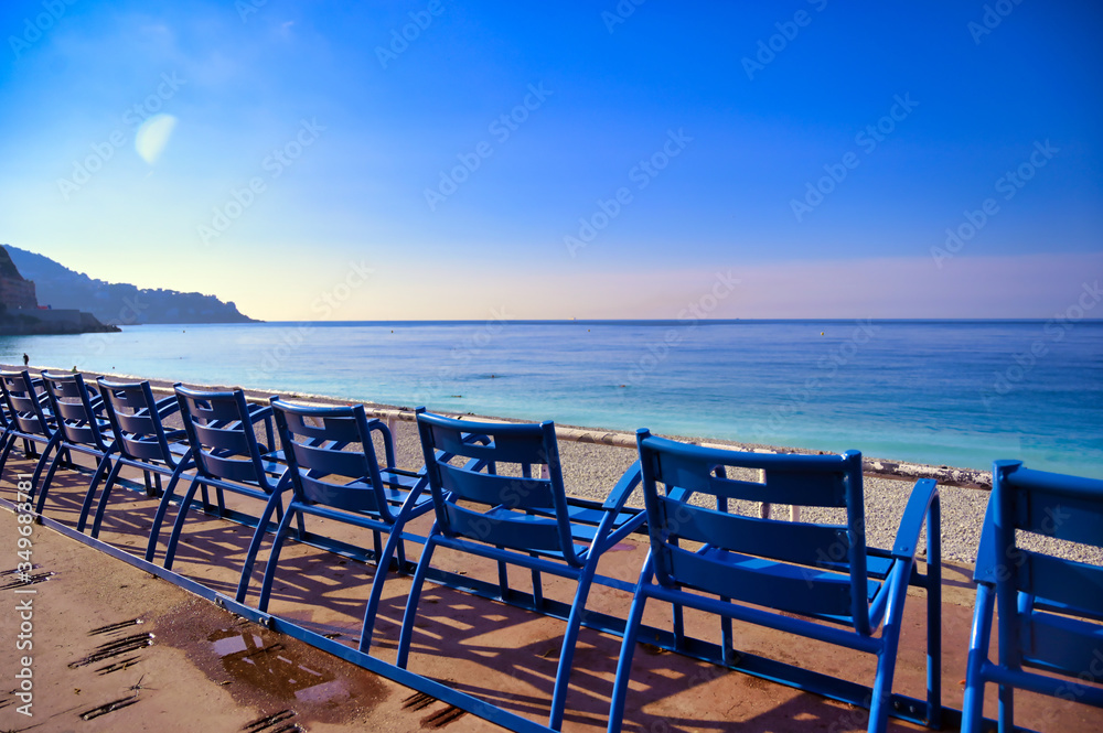 Blue chairs along the Promenade des Anglais on the Mediterranean Sea at Nice, France along the French Riviera.