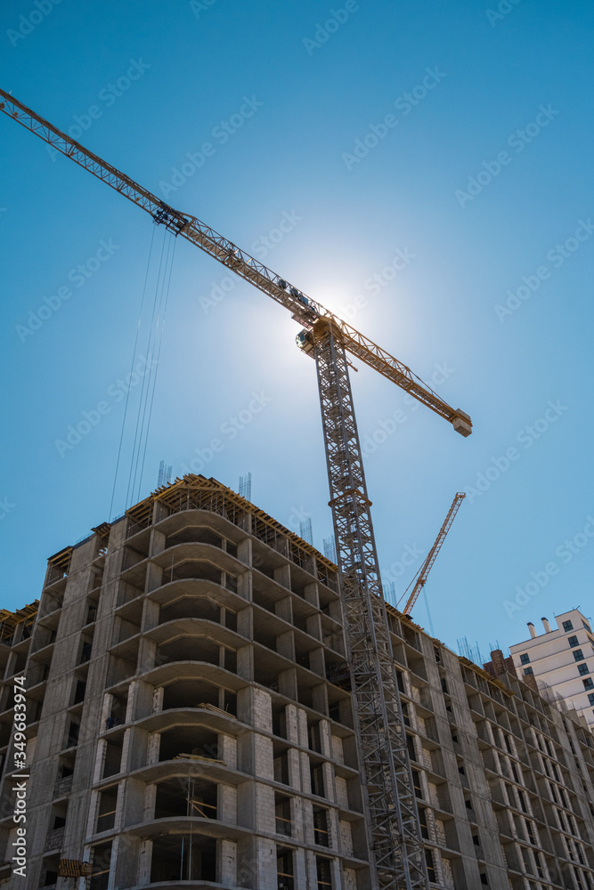 Construction of a new multi-storey building. The facade building with windows and balconies. Tower crane working at construction site. Modern residential building architecture background Construction of a new multi-storey building. The facade building with windows and balconies. Tower crane working at construction site. Modern residential building architecture background