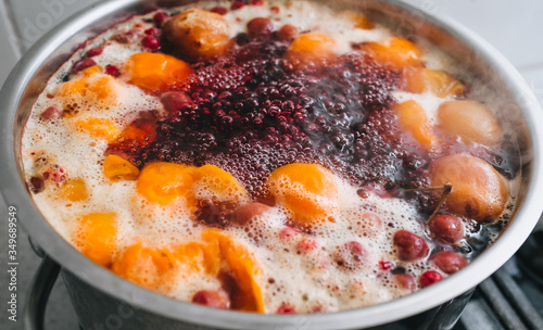 Fresh fruits are boiled in boiling water in a metal pan on the stove. Delicious stewed apricot, apples, cherries, raspberries. Photography, concept.