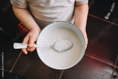 Little girl child holds in his hands a bowl with a spoon, dough, porridge. Photography, concept.