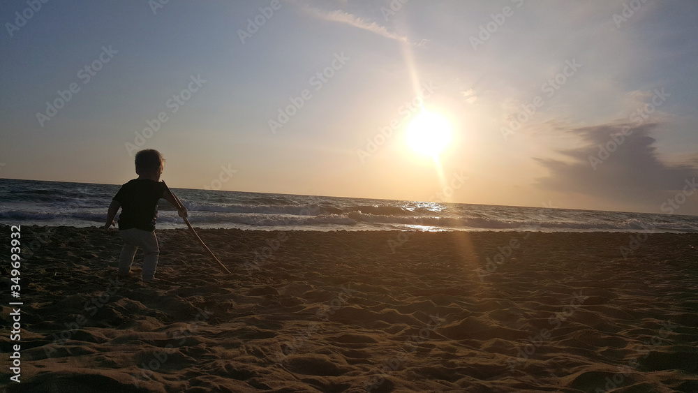 Little child playing in sand at sunset.