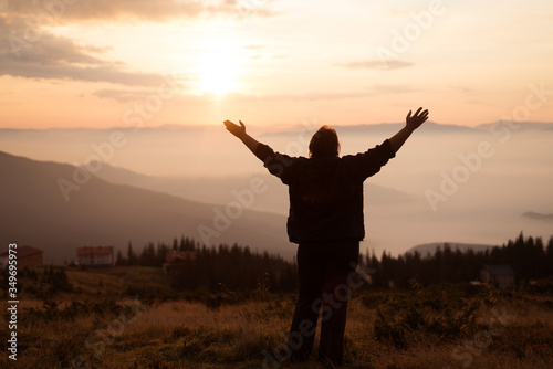  An elderly woman stands at full height and praying in the mountains, stretches her arms to heaven. Dawn in the mountains. Peace of mind. Hope. Appeasement. Integrity. Knowing yourself. Acknowledgment