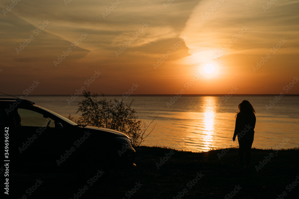 soft focus girl stands next to her car at dawn. The view from the back. Silhouette. The sun rises and the reflection falls on water. Loneliness. Privacy. The balance is inside. Good one with oneself.