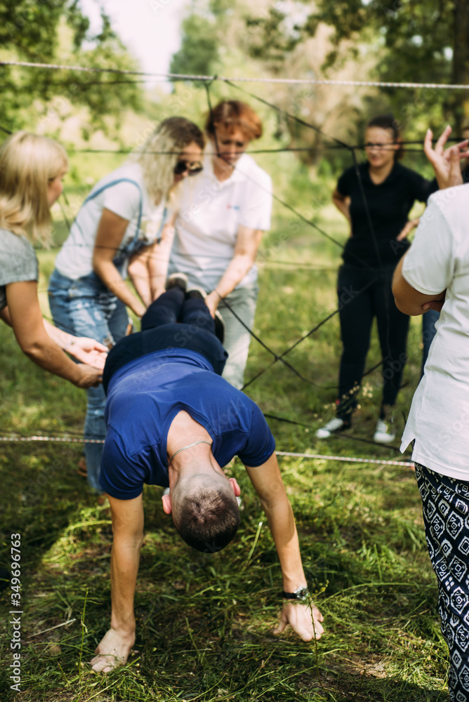 Fototapeta premium man in his arms climbs straight over the ropes and friends help him hold his legs. Team building activity. Confidence in colleagues in the team. Unity, togetherness