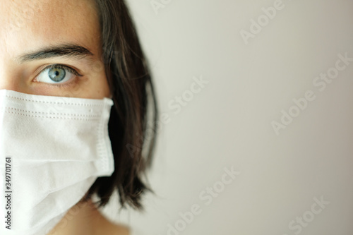 Close up of half the face of caucasian woman with blue eyes wearing a white face mask for protection during coronavirus outbreak