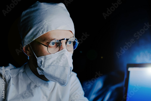 Male doctor scientist in uniform, glasses and a medical mask works at night in the office. professional look.