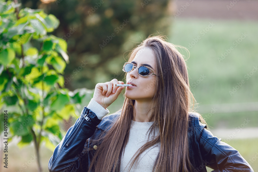 Beautiful woman in sunglasses smoking. A beautiful charming girl can't stop smoking a cigarette or tobacco. The beautiful girl blows tobacco smoke. She thinks about her future life and experience