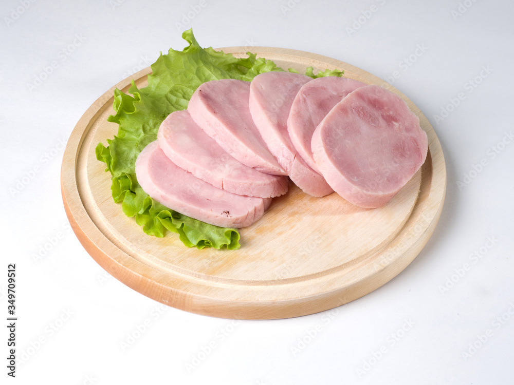 Ham sliced on a blackboard. Next to a leaf of lettuce