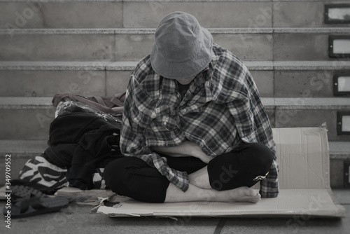 Homeless man sitting on the street in the shadow of the building. He begging for  help and money. Poverty concept. Black and white picture