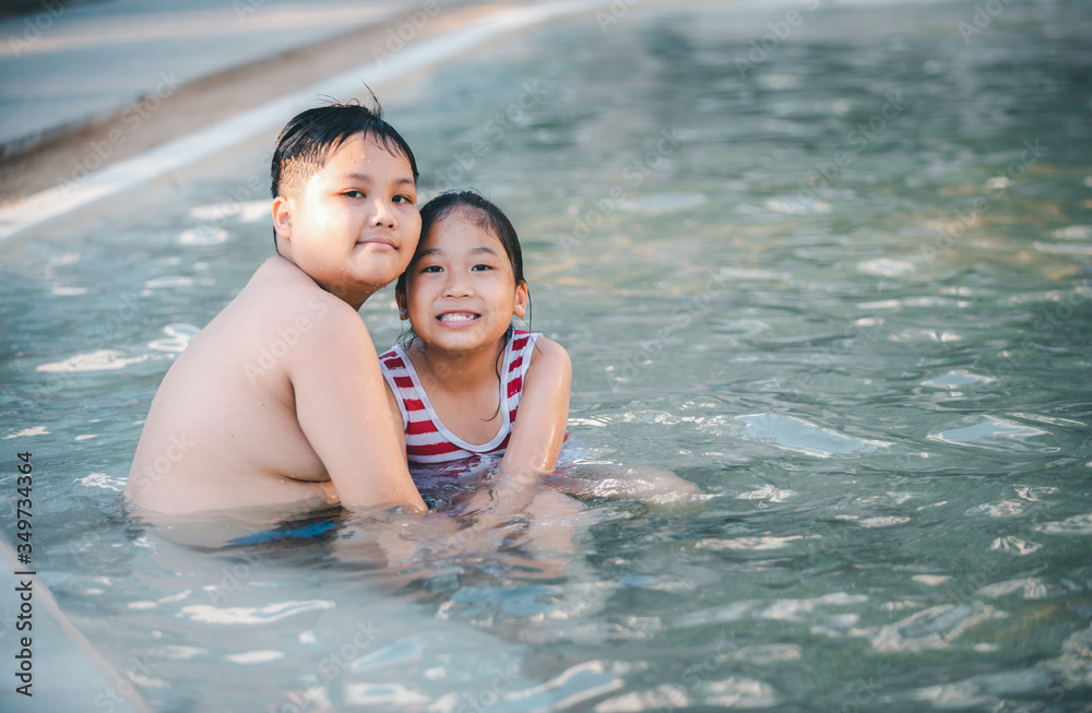 Happy brother and sisiter are playing water at swimming pool,