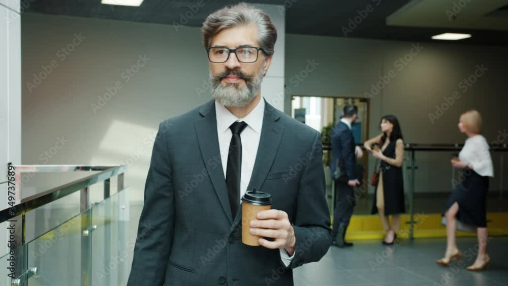 Portrait of mature man in suit walking in office building hallway with take out coffee wearing elegant suit and glasses. Employees and workplace concept. Portrait of mature man in suit walking in office building hallway with take out coffee wearing elegant suit and glasses. Employees and workplace concept.