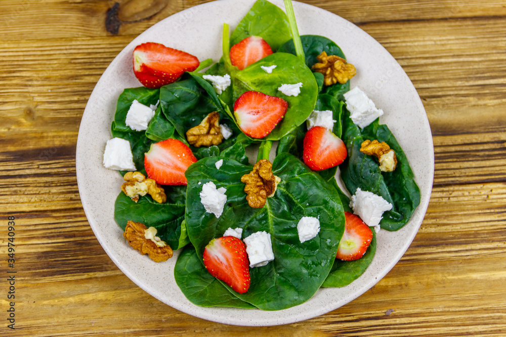 Fresh healthy salad with strawberry, spinach, walnuts and feta cheese on wooden table. Top view