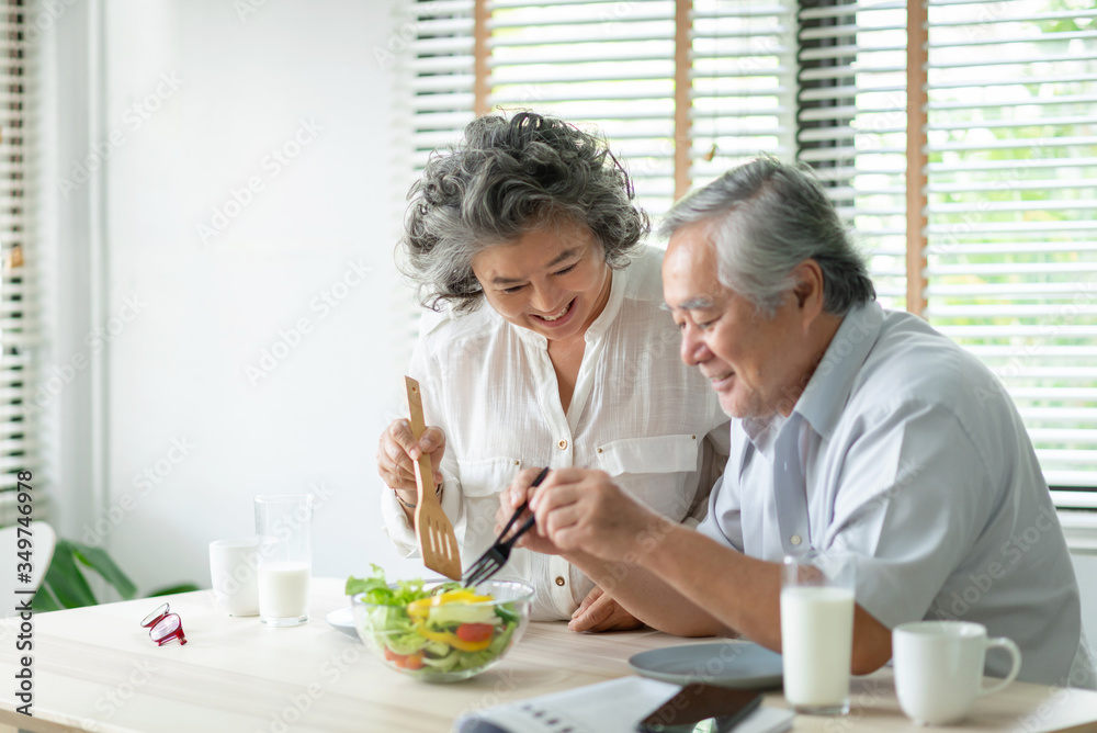 Happy Asian Older couple relaxing preparing and cooking healthy salad at home together. Romantic Senior man and woman smiling enjoying a meal.