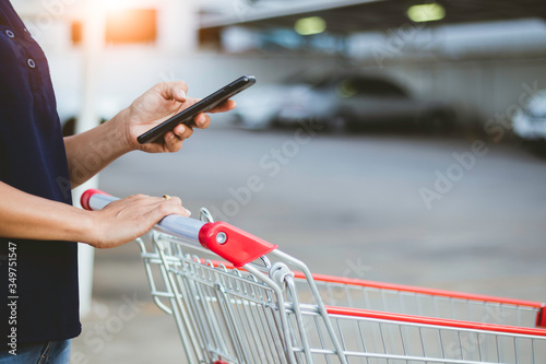 woman using smartphone and holding a cart shooping in the store.