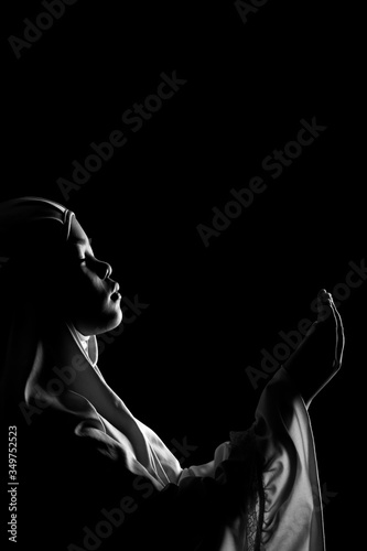 The image of an Asian Muslim girl who is praying with tranquility and faith, with the light from the studio lights from behind, with copy space. © maya1313