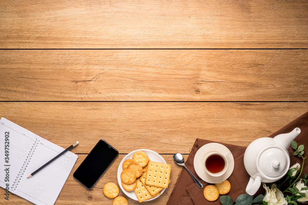Afternoon tea set with bread, crackers, and a mobile phone and a notebook beside on the wooden table, with copy space, top view.