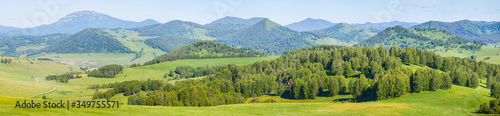 Panoramic mountain view. Bright sunlight, spring greens of forests and meadows.
