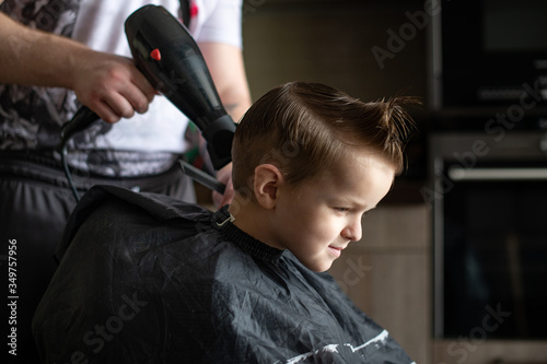 Barbershop and hairdressing at home. Men's and children's haircuts. The hairdresser cuts the boy. Stylish hairstyle for a child