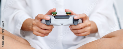 Closeup image of a woman holding game controller while playing games , sitting on a white cozy bed at home © Farknot Architect