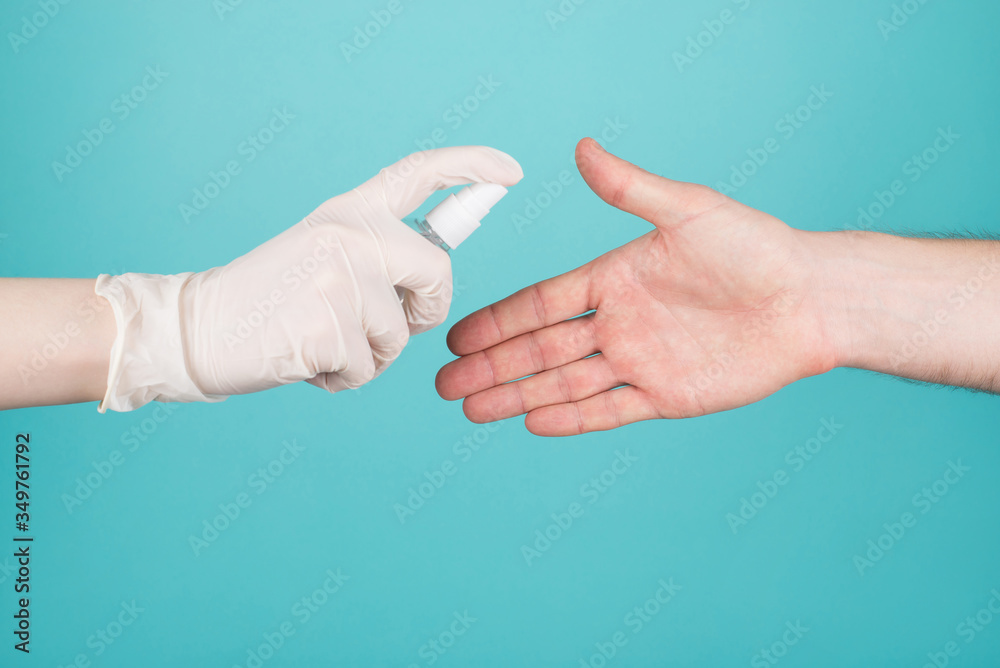 Stop spreading coronavirus patient concept. Cropped close-up photo of woman in gloves sprays sanitizer on man's hand isolated on blue teal turquoise background